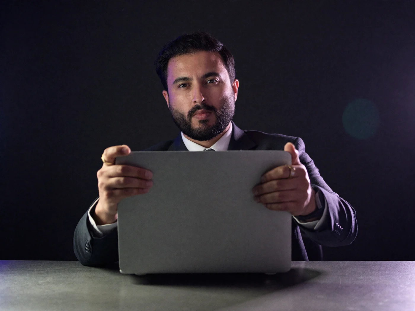 Nikhil Sharma sliding an open laptop across a desk toward the viewer