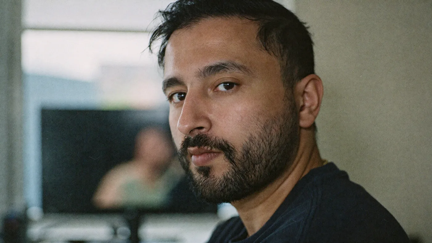 Nikhil Sharma in close portrait, turned toward the camera, a monitor out of focus behind him